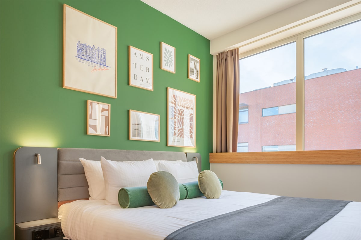Maxhotel-Superior-Room-1-min A superior double hotel room with a large bed, green wall, and framed artwork.