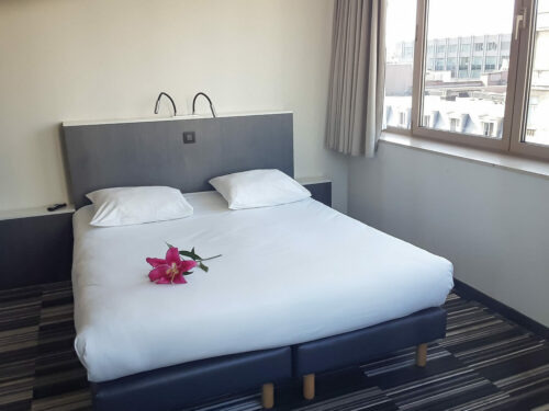 Hotel room with a double bed decorated with a pink flower and a view over the city of Brussels