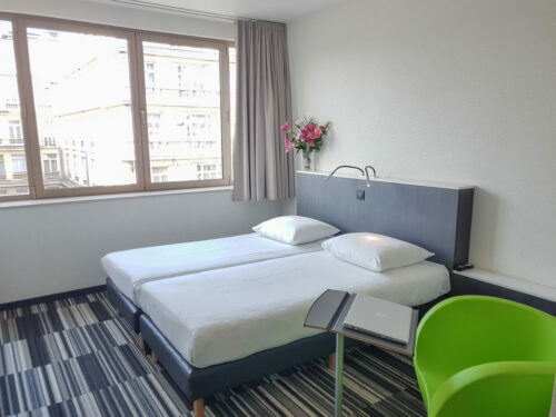 Hotel room with a double bed, flowers and a green chair with a small working desk