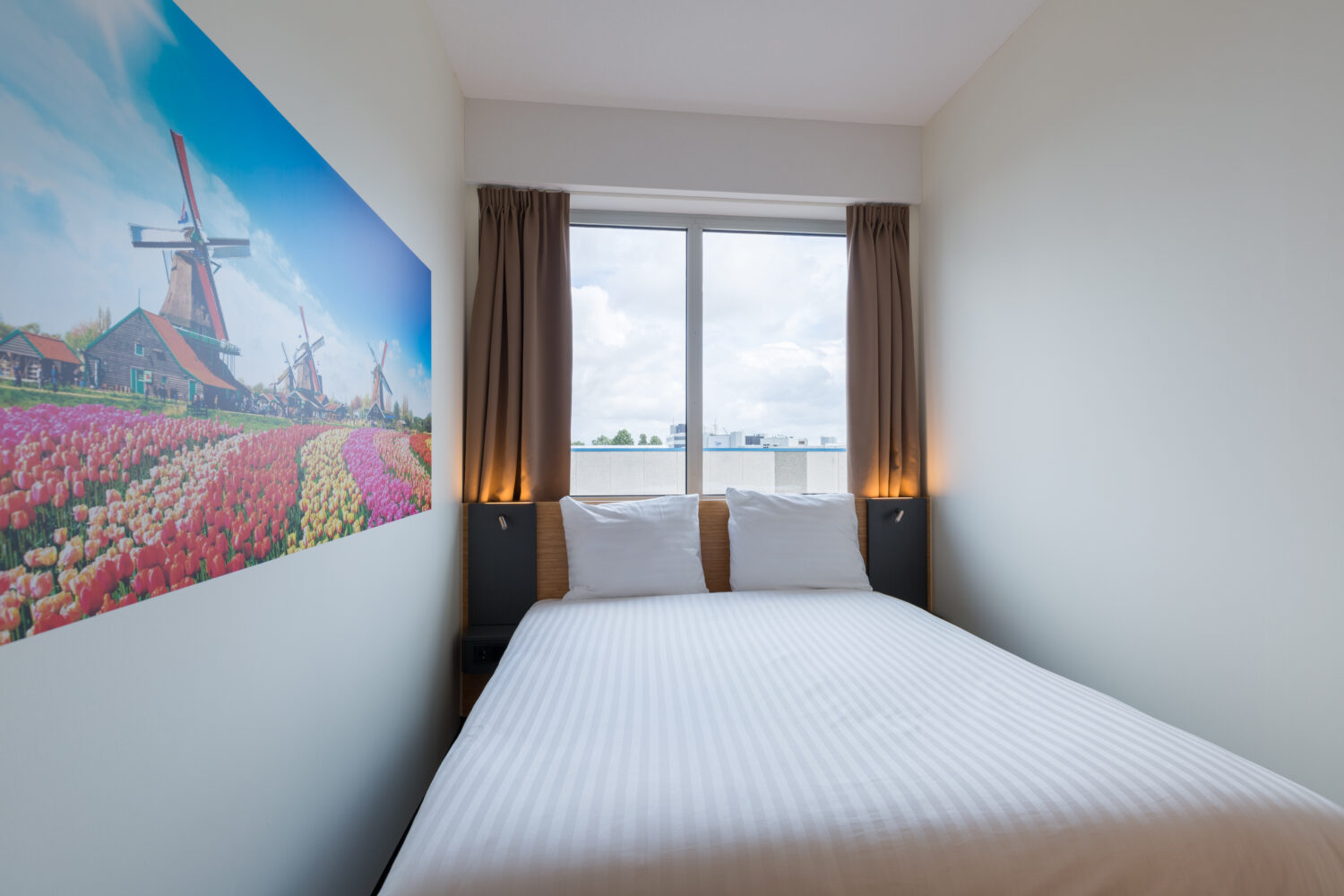 Small hotel room with a bed and picture of a flower field