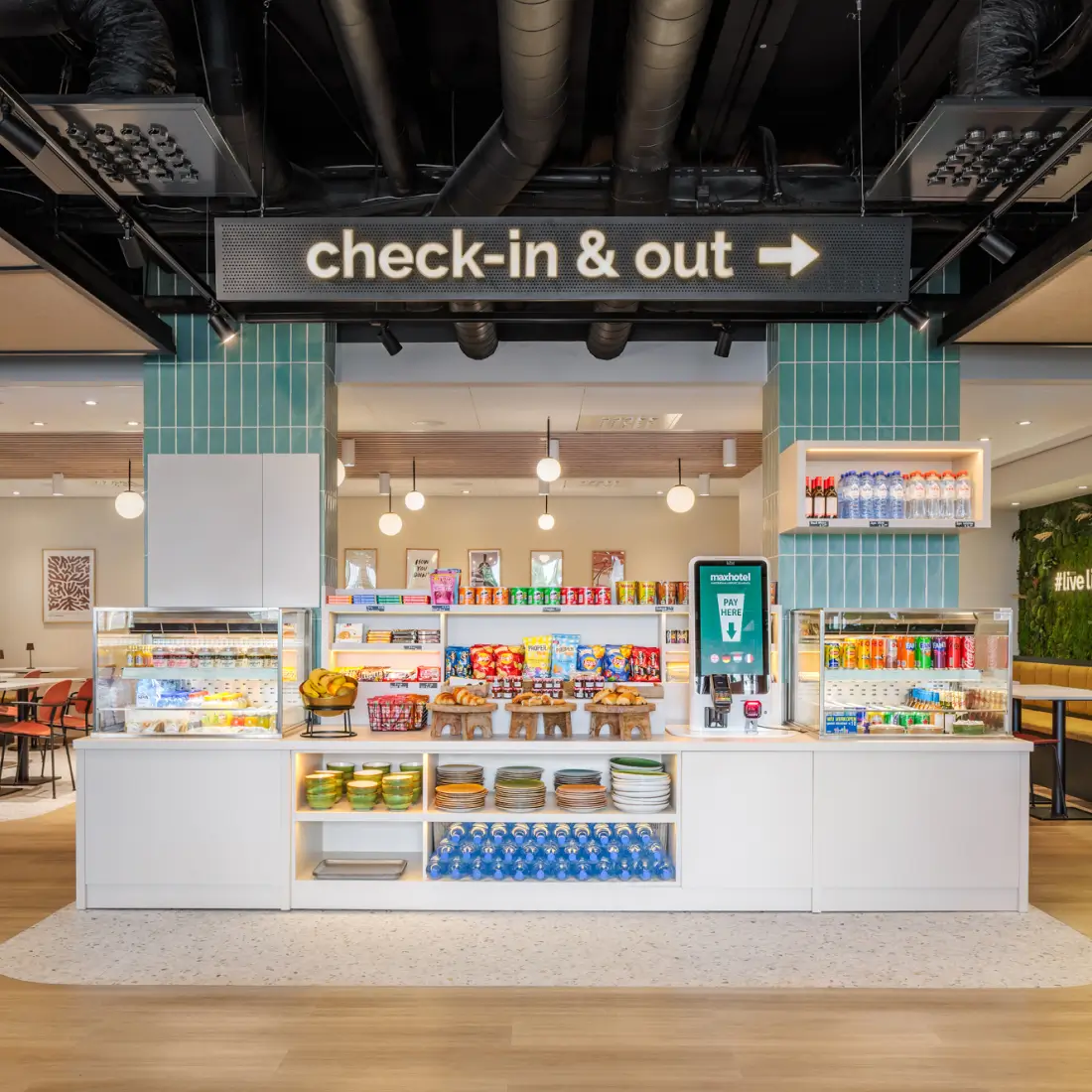 De in- en uitcheckbalie van het Maxhotel met snacks, drankjes en een zelfbedieningsstation.