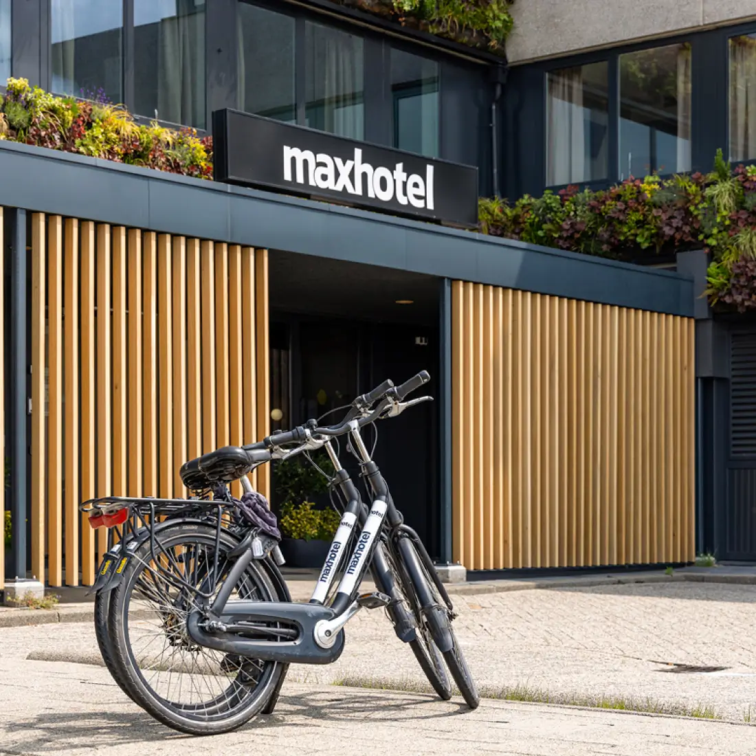 Dutch bicycles parked outside Maxhotel entrance with wooden slat facade and sustainable green planters
