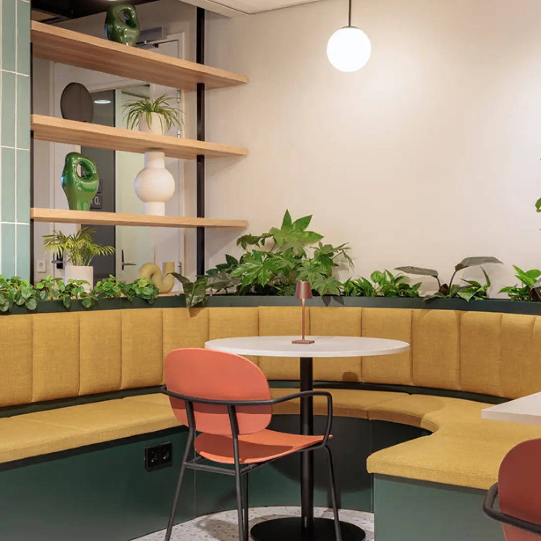 Maxhotel lounge seating area with curved banquette, plants, and workspace for relaxing guests